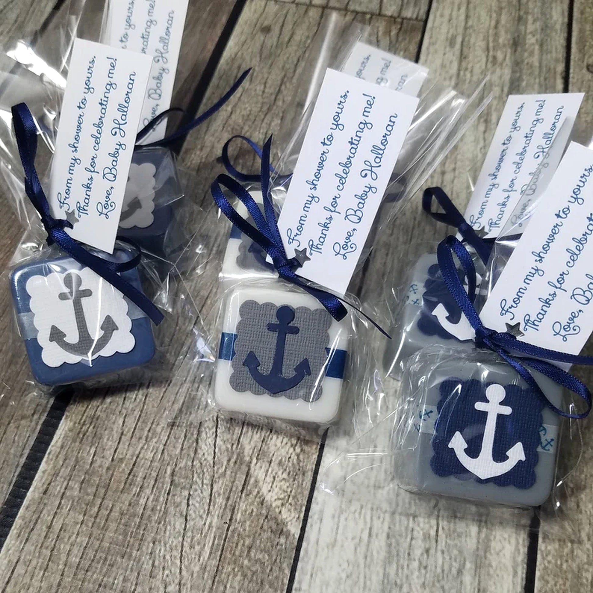 Small square Soaps with anchor design, wrapped in clear plastic with blue ribbons and labels on a wooden surface.
